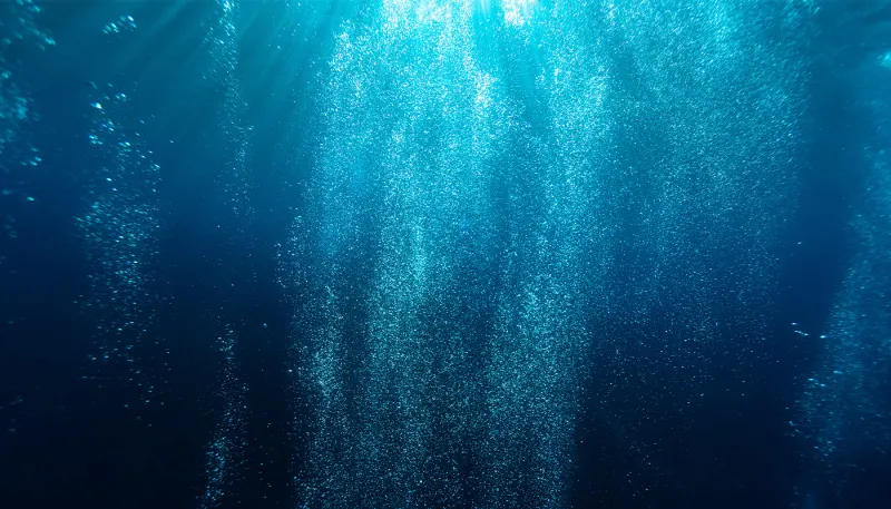 Deep blue underwater scene with light rays and rising bubbles